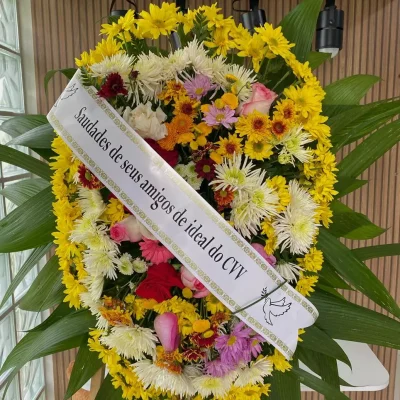 Coroa de flores 3003 para funeral com margaridas amarelas, rosas, crisântemos coloridos e faixa de homenagem personalizada.