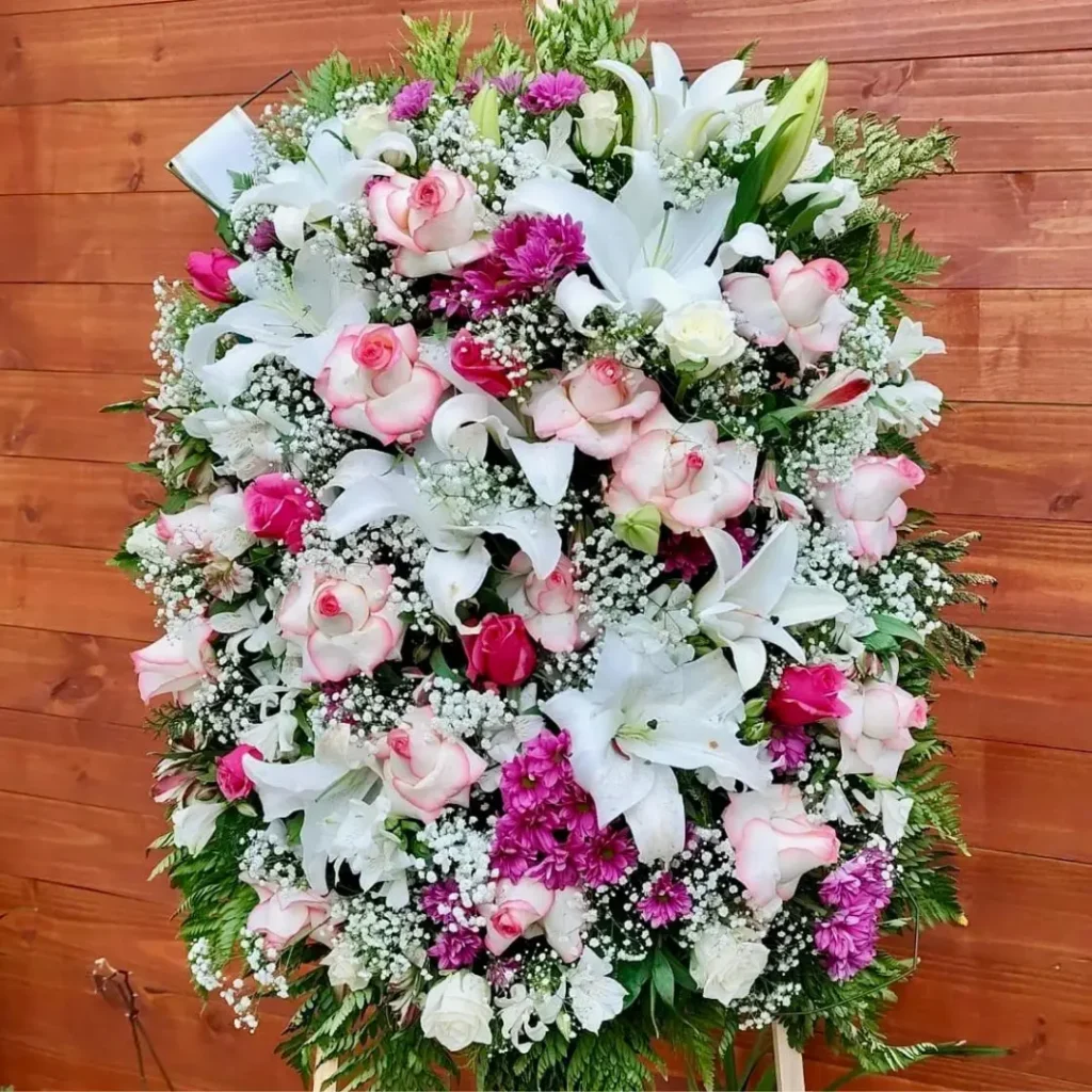 Coroa Super Luxo Cod 35 com rosas cor-de-rosa, lírios brancos, flores roxas e folhagens verdes, simbolizando amor, respeito e despedida.