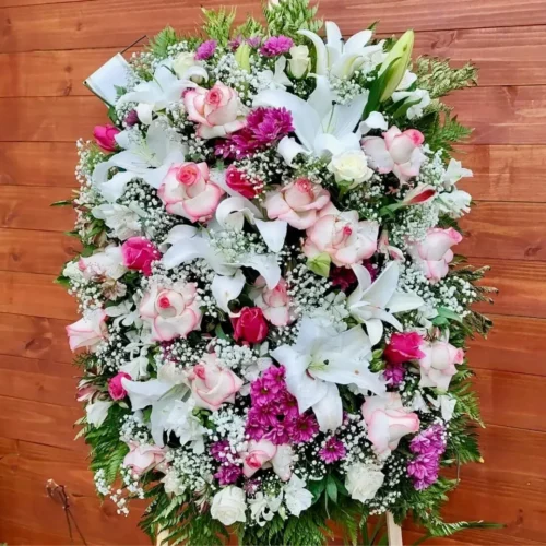 Coroa Super Luxo Cod 35 com rosas cor-de-rosa, lírios brancos, flores roxas e folhagens verdes, simbolizando amor, respeito e despedida.