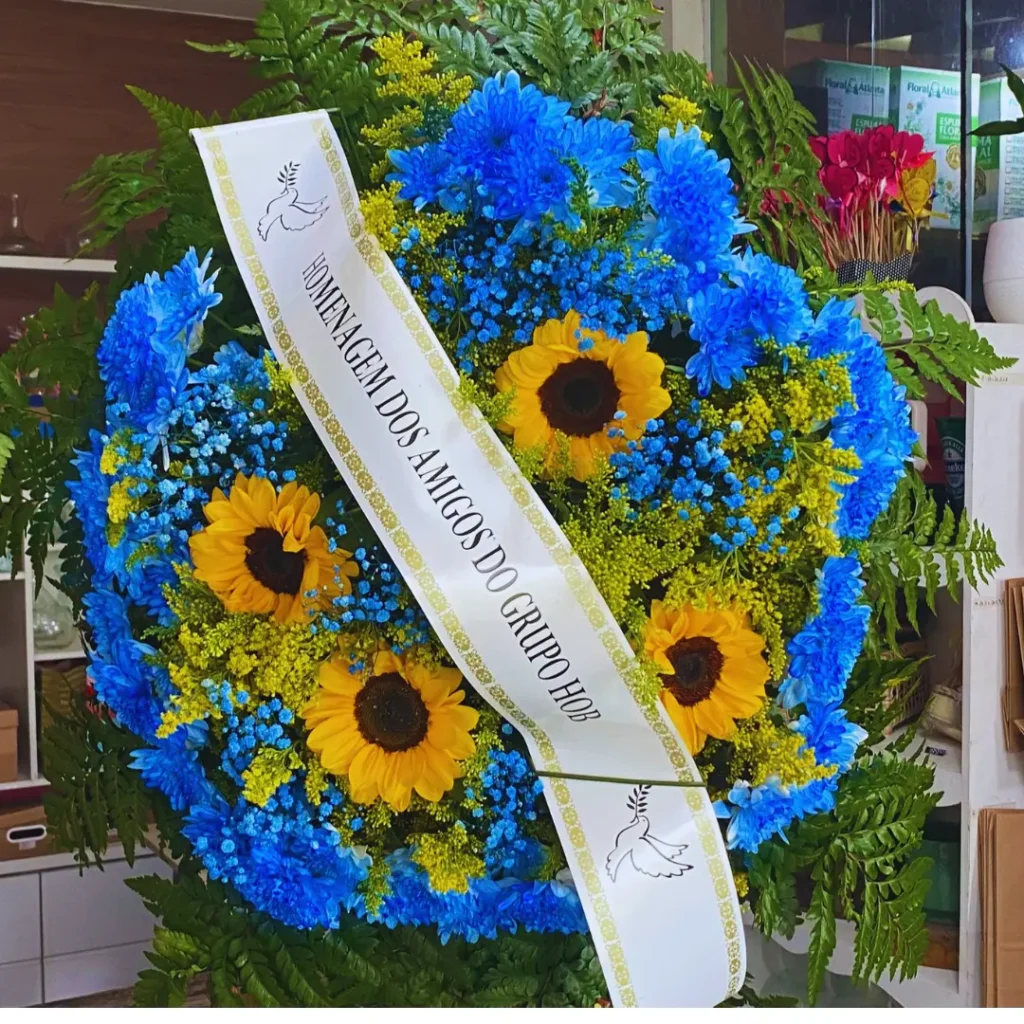 Faça a sua homenagem com nossa Coroa de flores cod 38 é montanda com crisântemos naturais tingidos de azul e Girassóis.